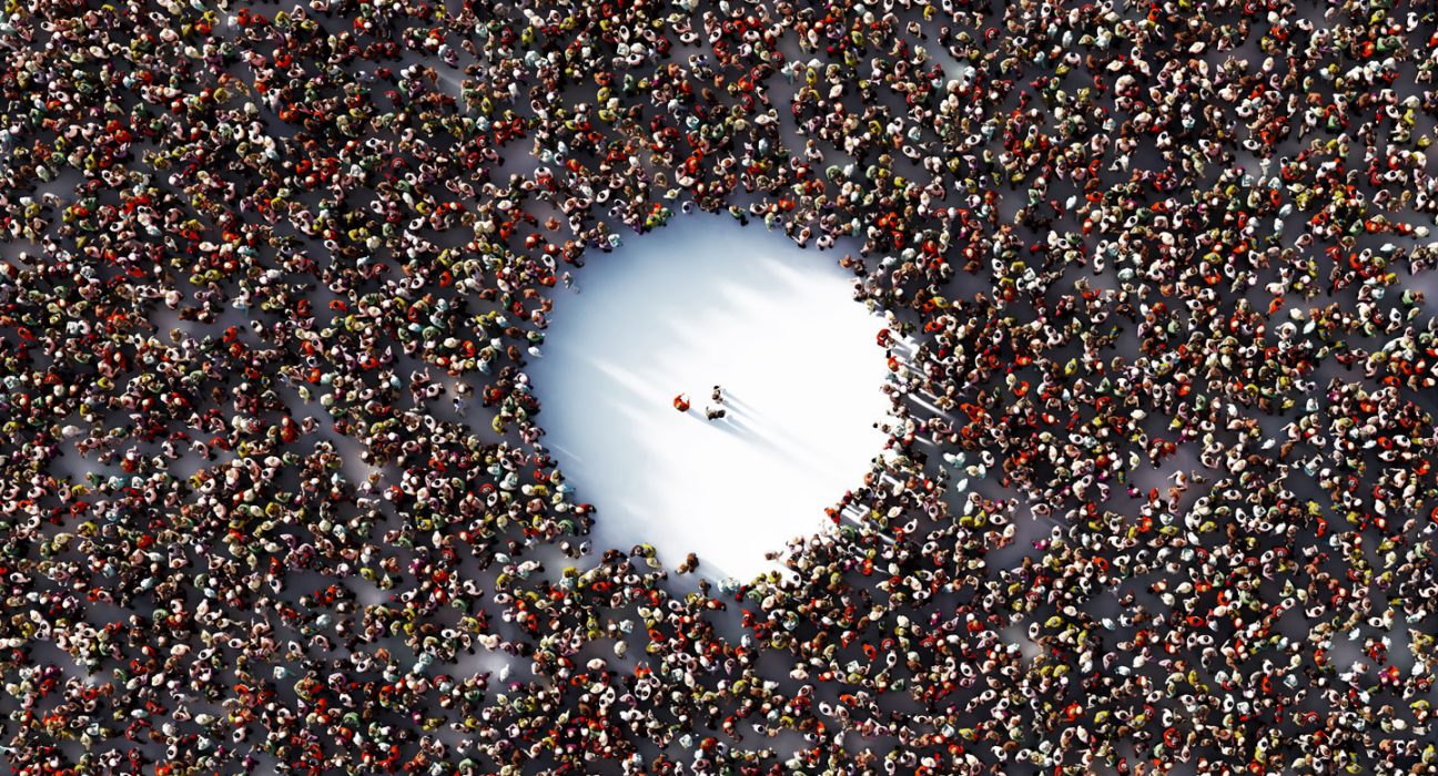 A packed crowd with a giant empty circle in the middle is shown from above. Three people stand in the empty space..