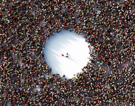 A packed crowd with a giant empty circle in the middle is shown from above. Three people stand in the empty space..