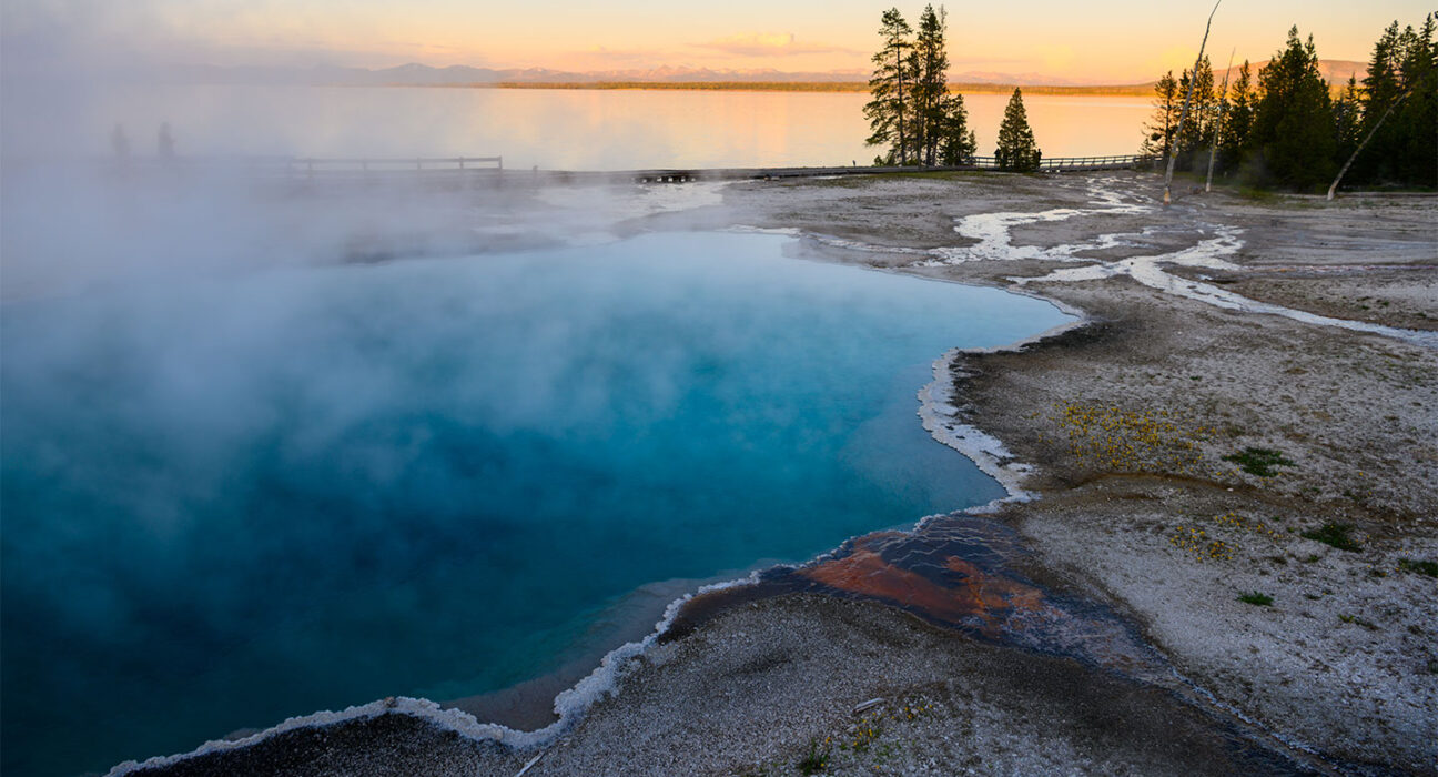 a clear pool of water with crystals at the edges is steaming as the sun sets