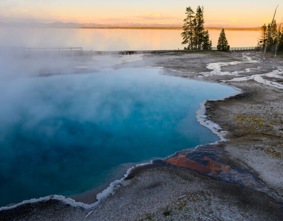 a clear pool of water with crystals at the edges is steaming as the sun sets