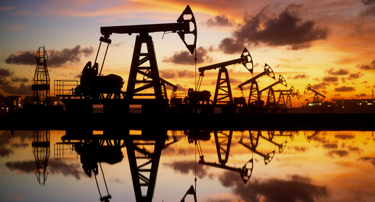 The silhouette of oil rigs among an orange and blue sky.