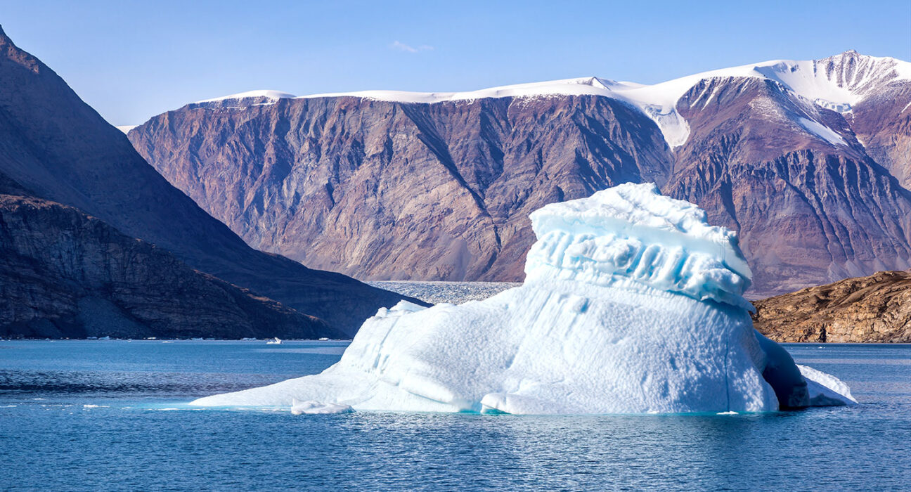 a photo of Dickson Fjord, a small iceberg is in ocean water close to steep snow covered cliffs