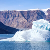 a photo of Dickson Fjord, a small iceberg is in ocean water close to steep snow covered cliffs