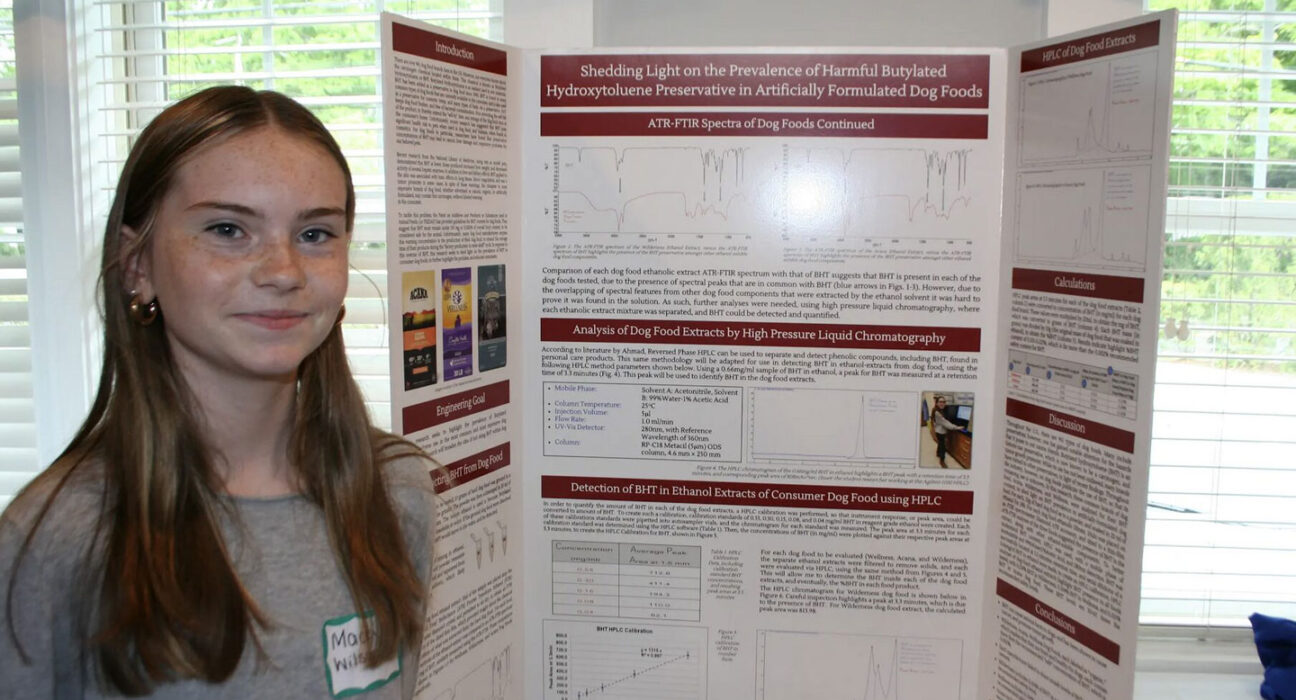 a photo of Mackensey Wilson, a young girl with pale skin, freckles and straight hair standing next to her science project poster board about finding BHT in pet food