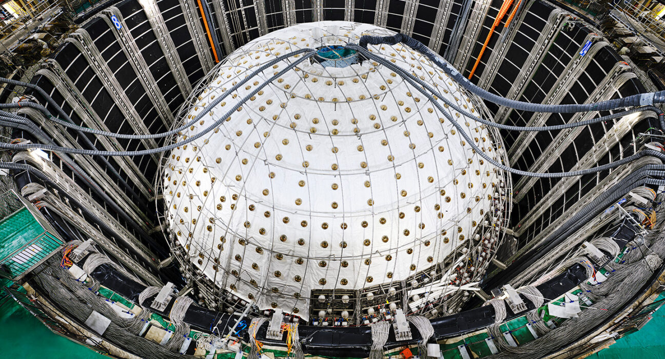 A sphere inside a large pit is covered in white sheeting with tubes entering a hole in the top.