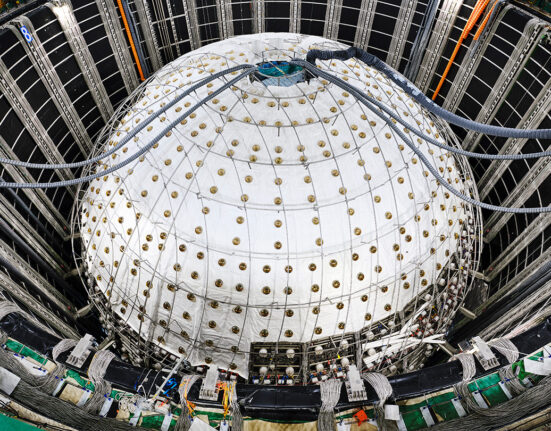 A sphere inside a large pit is covered in white sheeting with tubes entering a hole in the top.