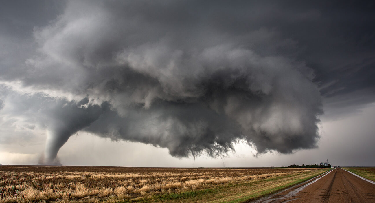 Dark storm clouds hover over a field as a large tornado touches down.